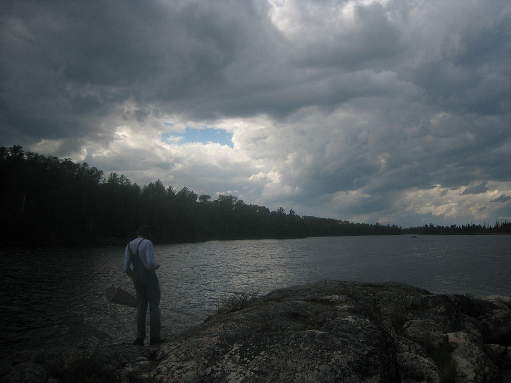 Zeke Kingsbury'25 standing & reflecting in front of a lake on a cloudy day. 