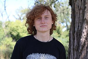 Student, Zeke, smiling at the camera with nature in the background.
