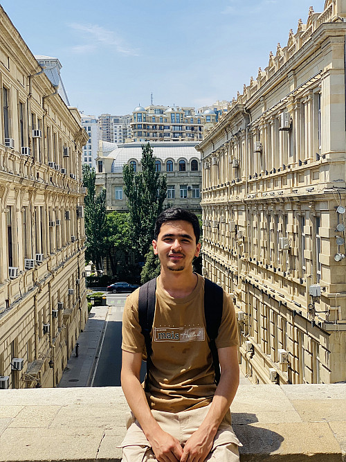 A student sitting with a building in the background.