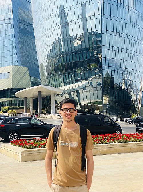 A student is standing in front of the curved, mirrored office towers on a sunny day.
