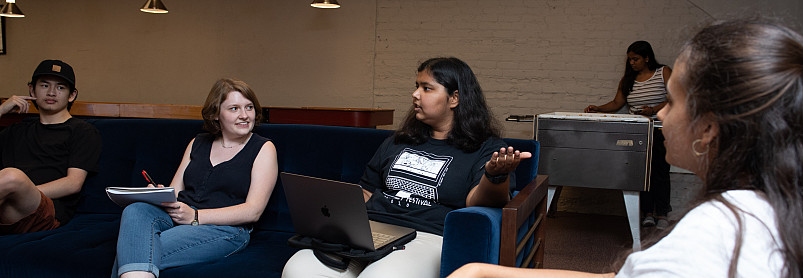 Four students are seated on a couch and an armchair, talking.