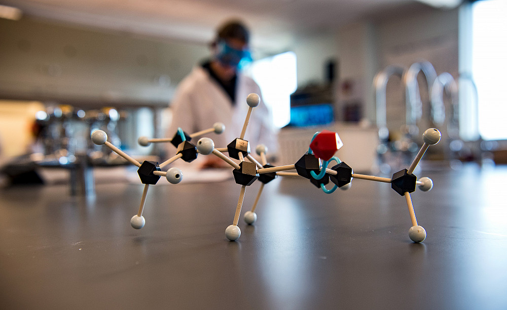 A model of a molecule sitting on a lab desk in front of a student doing laboratory work.
