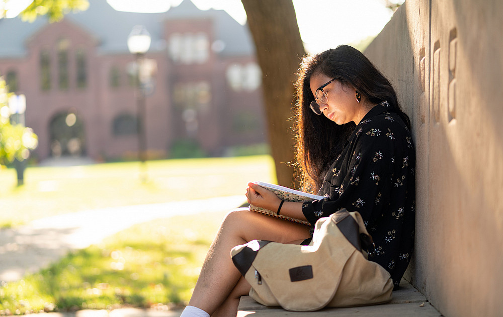 A Beloit College student looks through a journal on a stone bench in the sunshine.