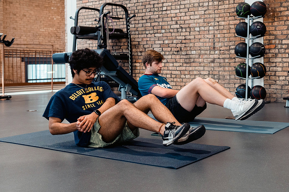 Two Beloit College students exercise together on mats on the fitness floor of the Powerhouse student center.