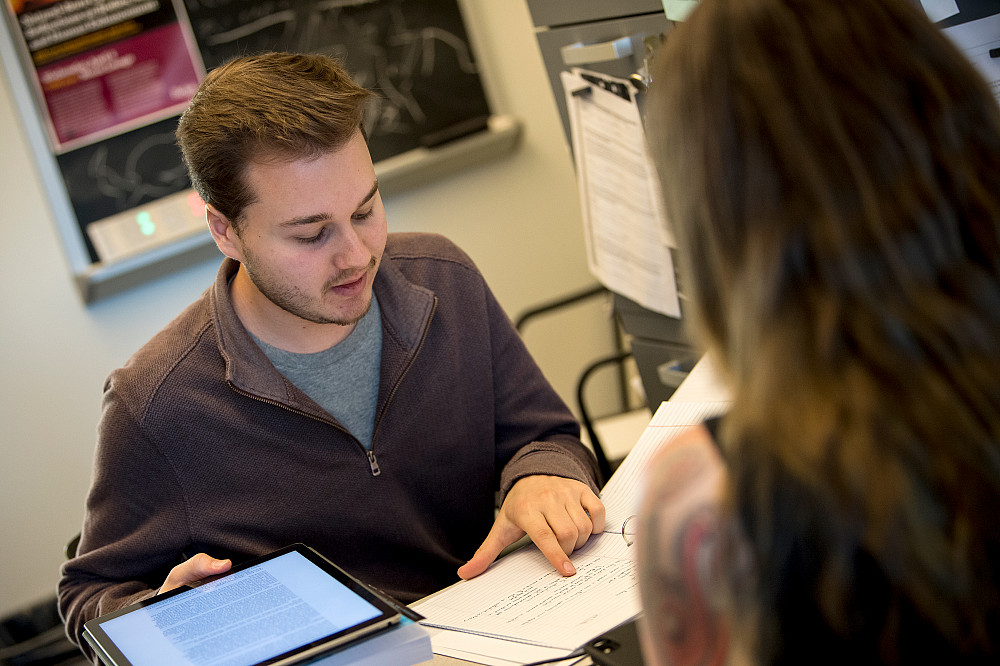 A Beloit College student works with another person over documents on paper and a tablet.