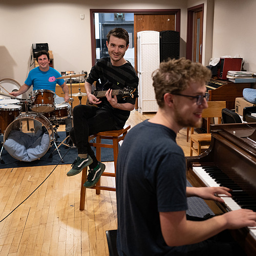 Three students play drums, guitar, and piano in the Maple Tree Studio.