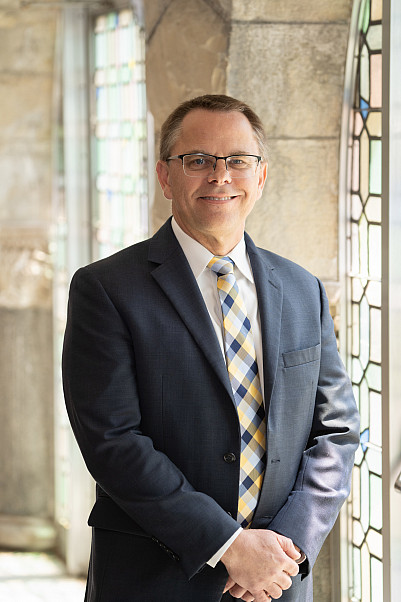 President Eric Boynton stands next to the stained glass doorways in Eaton Chapel.