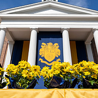 The commencement stage in front of Middle College, with a banner with the college seal and yellow mums.