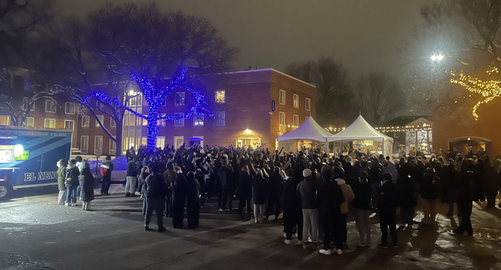 Many students are standing outside near the wall, with lights, tents, and taco trucks.
