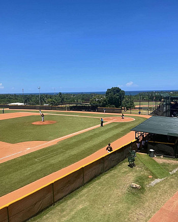 A view from a hill of a baseball field with people playing a game.