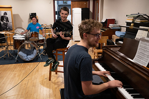 Three students play drums, guitar, and piano in the Maple Tree Studio.
