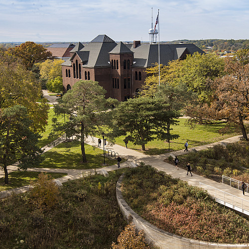it is a sunny autumn day and a red brick building with a dark roof is shown.
