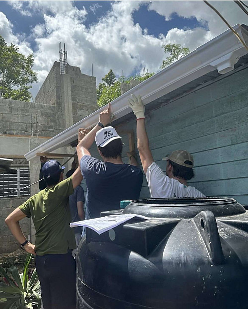 Three people hold up a gutter/pipe.