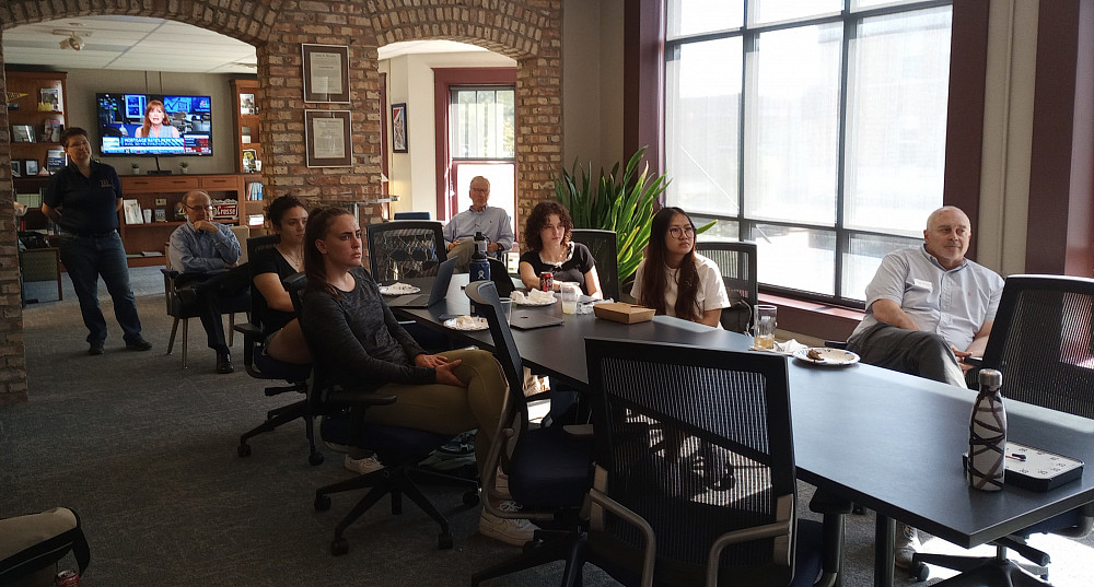 several people sit at a conference table and one person stands behind it.