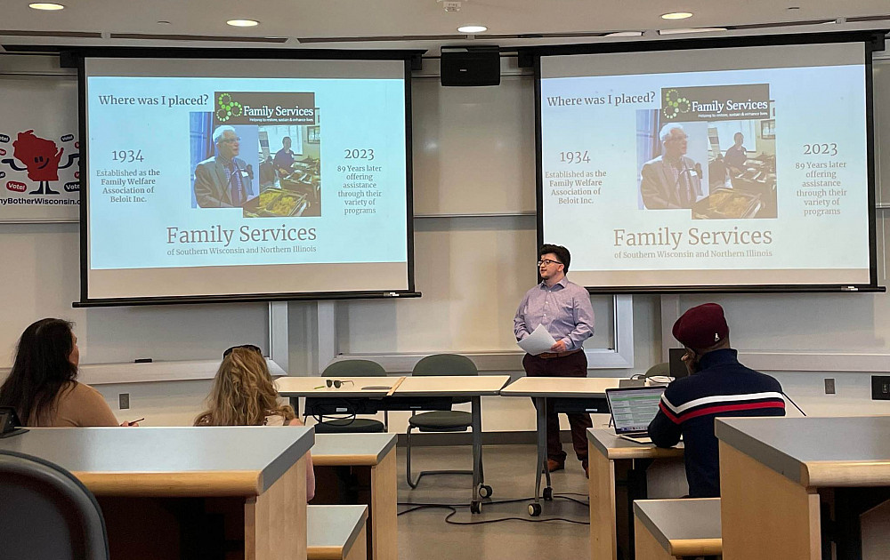 student standing in front of presentation that describes his placement site at Family Services of Southern Wisconsin and Northern Illinois