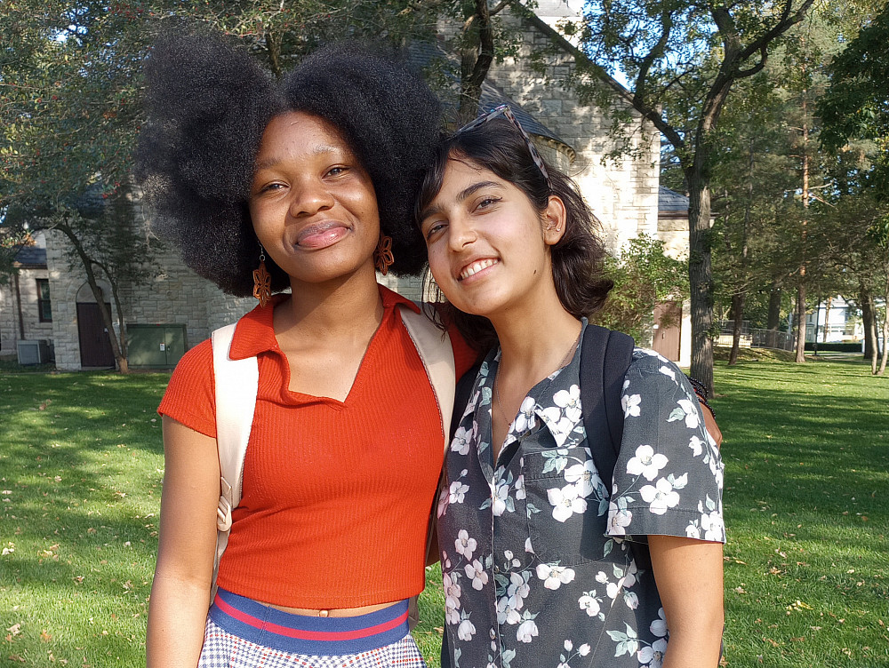 two smiling women stand next to each other with their arms around each other outside