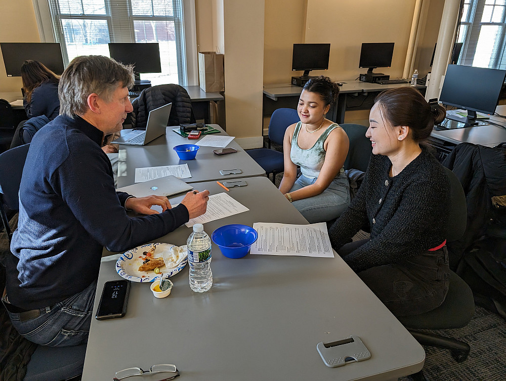 man sitting on the left with a pencil and paper and two smiling women on the other side of the table