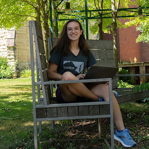 student sitting on a bench in the poetry garden with green foliage around