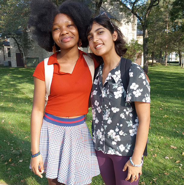 two smiling women stand next to each other with their arms around each other outside