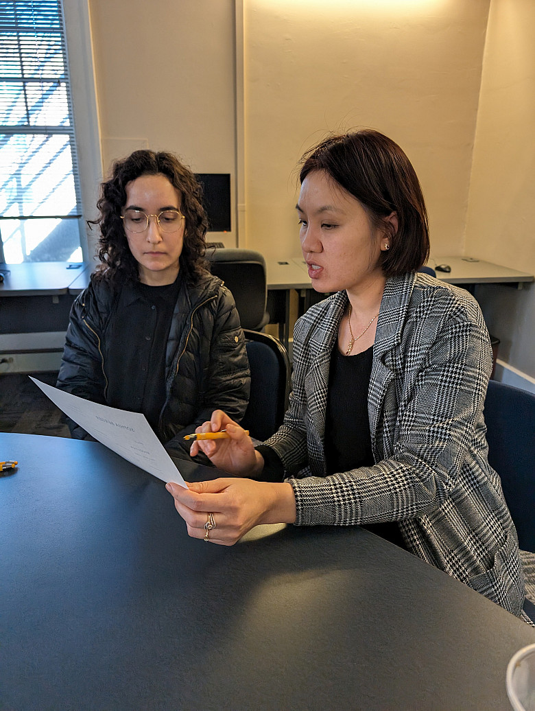 one person holds a piece of paper in their hand and the person next to her looks on