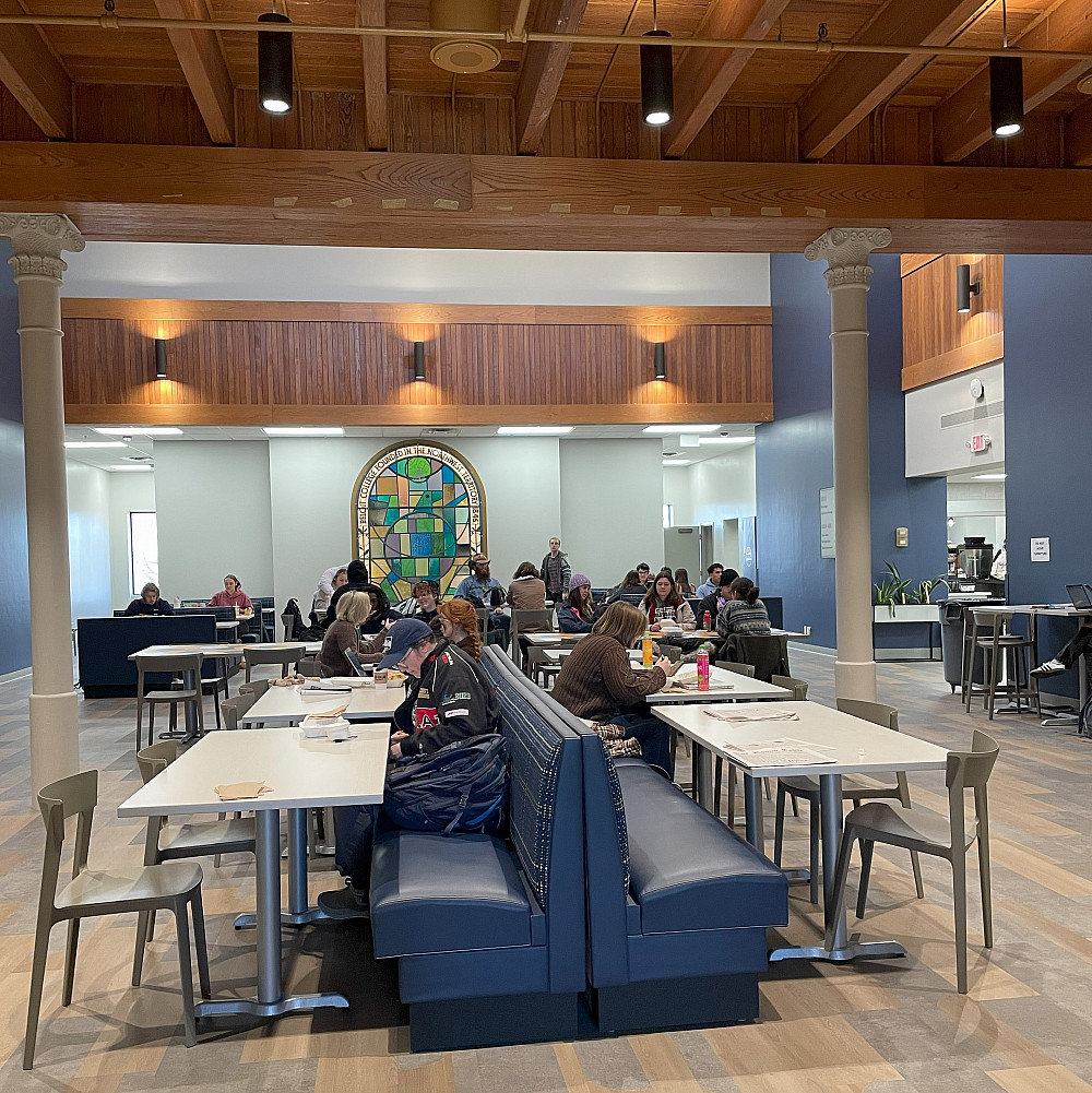 students are sitting at tables in the eating areas with their lunches.