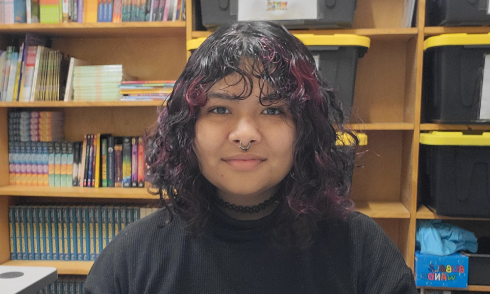 Olivia Alvarado'25 sits in front of a bookshelf and looks at the camera.