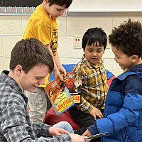 A student is sitting and reading to 3 elementary school students.