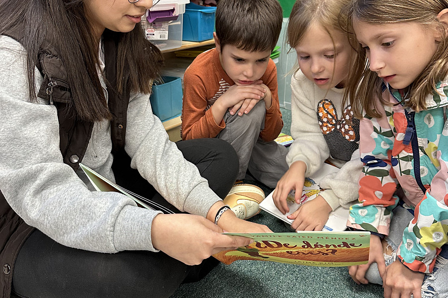 Rosa Solis'26 reads ¿De dónde eres? to three Todd Elementary students.