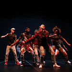 Dancers in worn clothing dancing on stage.