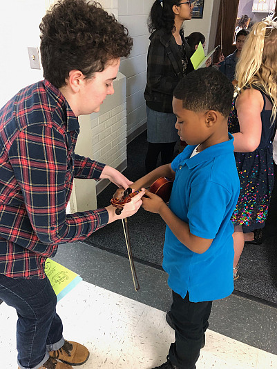 A Turtle Tunes teacher shows a student the proper hand position for a violin.