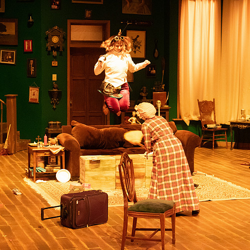 Ms. Holmes jumping on the couch while Ms. Watson tries to tidy up around her.