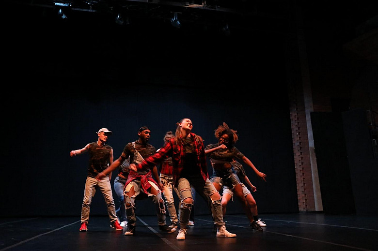 Dancers in worn clothing dancing on stage.