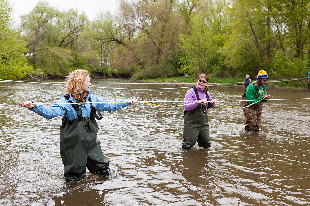 Three students test the water movement of a stream during their field study for a hydrogeology class.