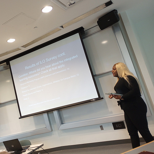 [a student stands in front of projected slides delivering a symposium presentation]