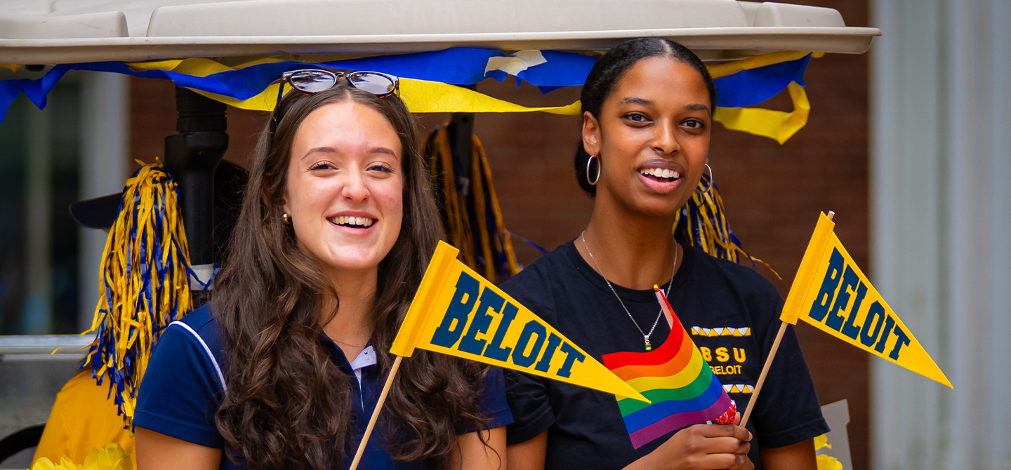 Two students holding Beloit College flags on the back of a golf cart.