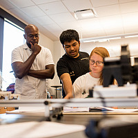 Physics Professor Obioma Ohia observes students as they discuss a class project.