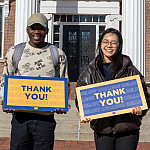 Two Beloit College students stand in front of Middle College, smiling, holding signs reading Thank you!