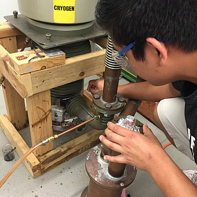 A student works with the cryogenic plumbing of a particle accelerator.