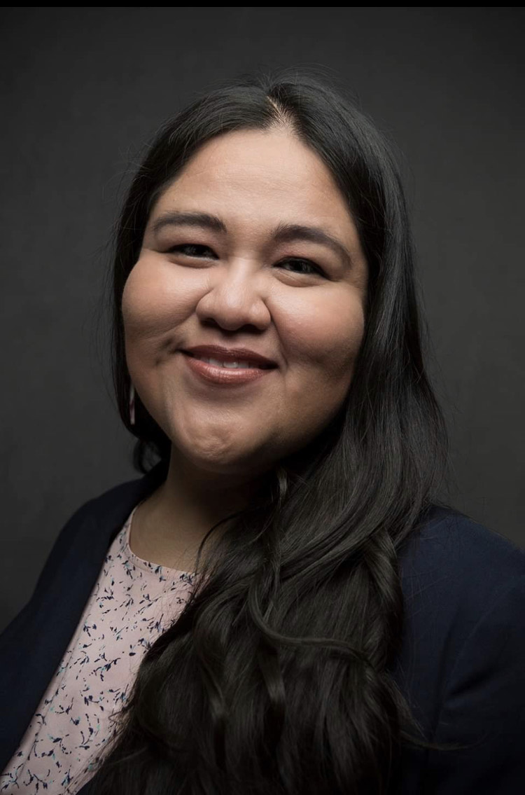portrait of a Native American woman with long black hair wearing a pink shirt and black blazer while smiling on a dark gray background