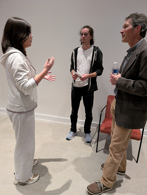 3 people are standing together. One is talking and two are listening.