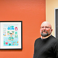 Joseph Derosier in a classroom in WAC with a print by illustrator Myriam au Citron