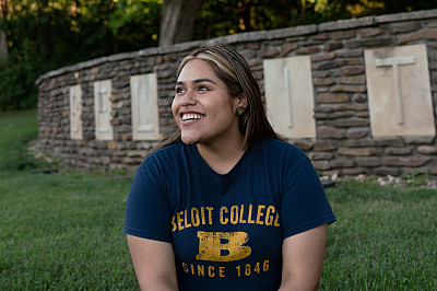 A student in Beloit gear sits in front of the Beloit College sign at the southwest side of campus...
