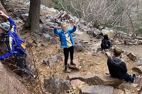 Students rest on a cliffside during a hike, with one student showing their enthusiasm.