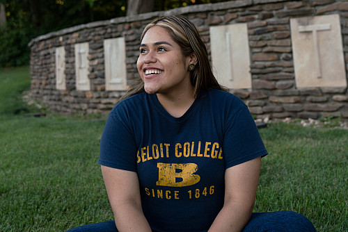 A student in Beloit gear sits in front of the Beloit College sign at the southwest side of campus.