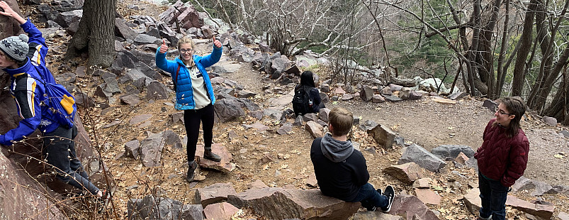 Students rest on a cliffside during a hike, with one student showing their enthusiasm.