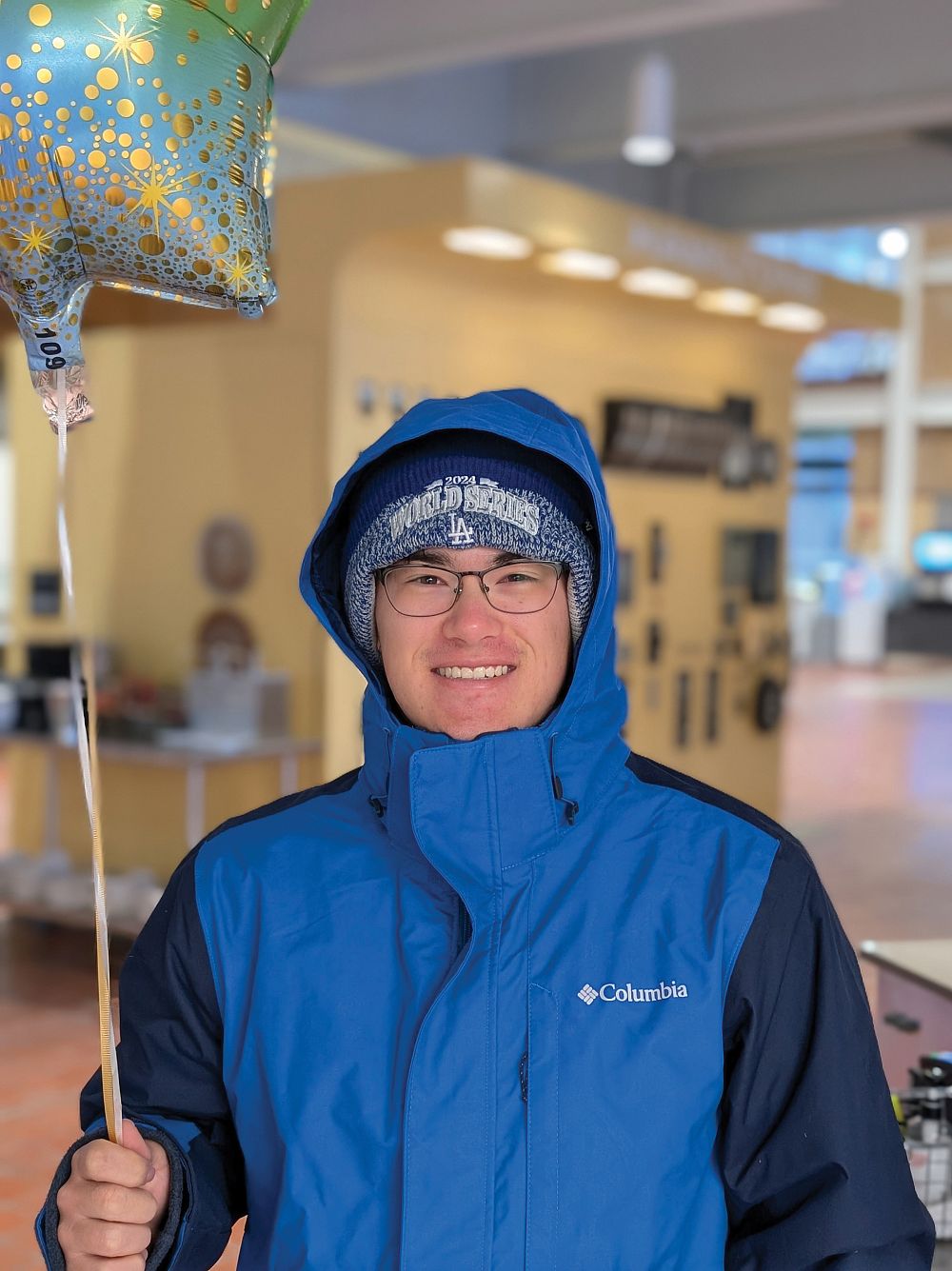 Ryan Ulmen '28, the first student to arrive for food on the opening of Hamiltons Commons, holds a balloon and smiles.