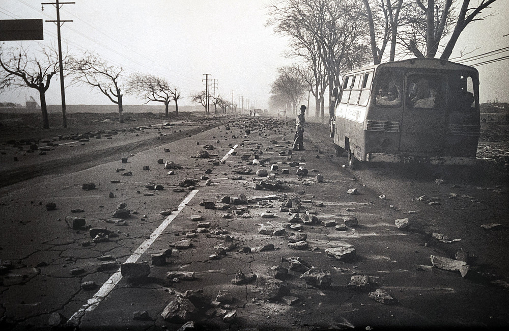A person stands outside of a bus on an empty road.