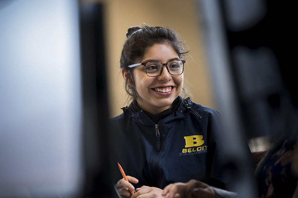 A student smiles, working with a group in a computer lab.