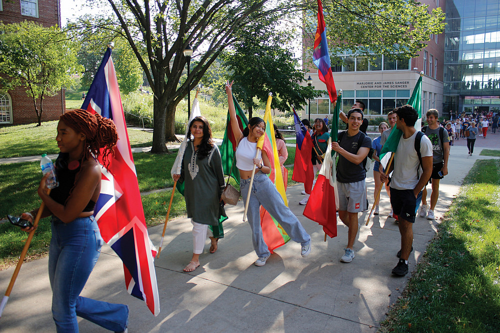 International students lead the Fall 2023 convocation parade, their country's flag in hand.