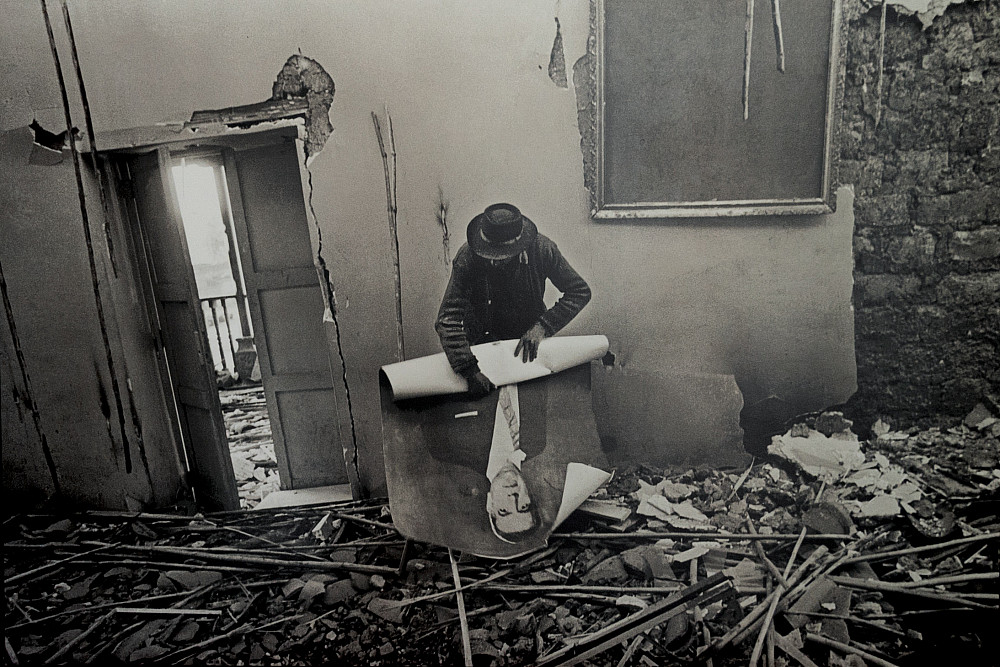 A victim of violence rolls up a poster in the midst of rubble.